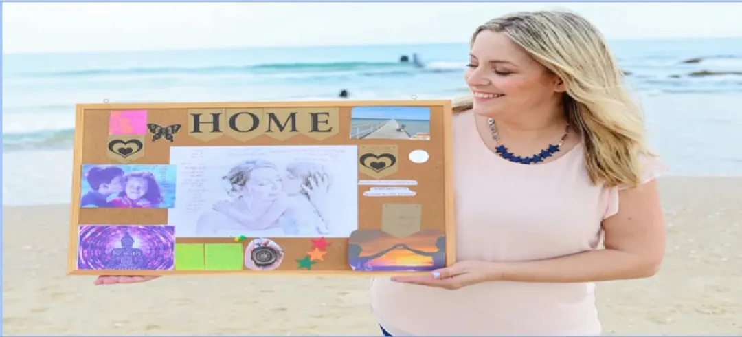 ים אוריה שליו מחזיקה לוח חזון עם המילה HOME על שפת הים